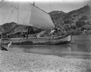 Photographie d'un bateau avec la voile déployée et un groupe d'équipage sur le dessus du bateau.