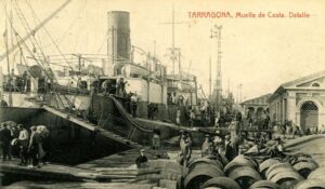 Vue du Moll de Costa avec un grand bateau à vapeur amarré où les marchandises sont chargées.
Sur l'esplanade du quai, bouteilles de vin et personnes au travail.
Carte postale : Détail du quai de la côte de Tarragone. Édité par Josep Anguela.