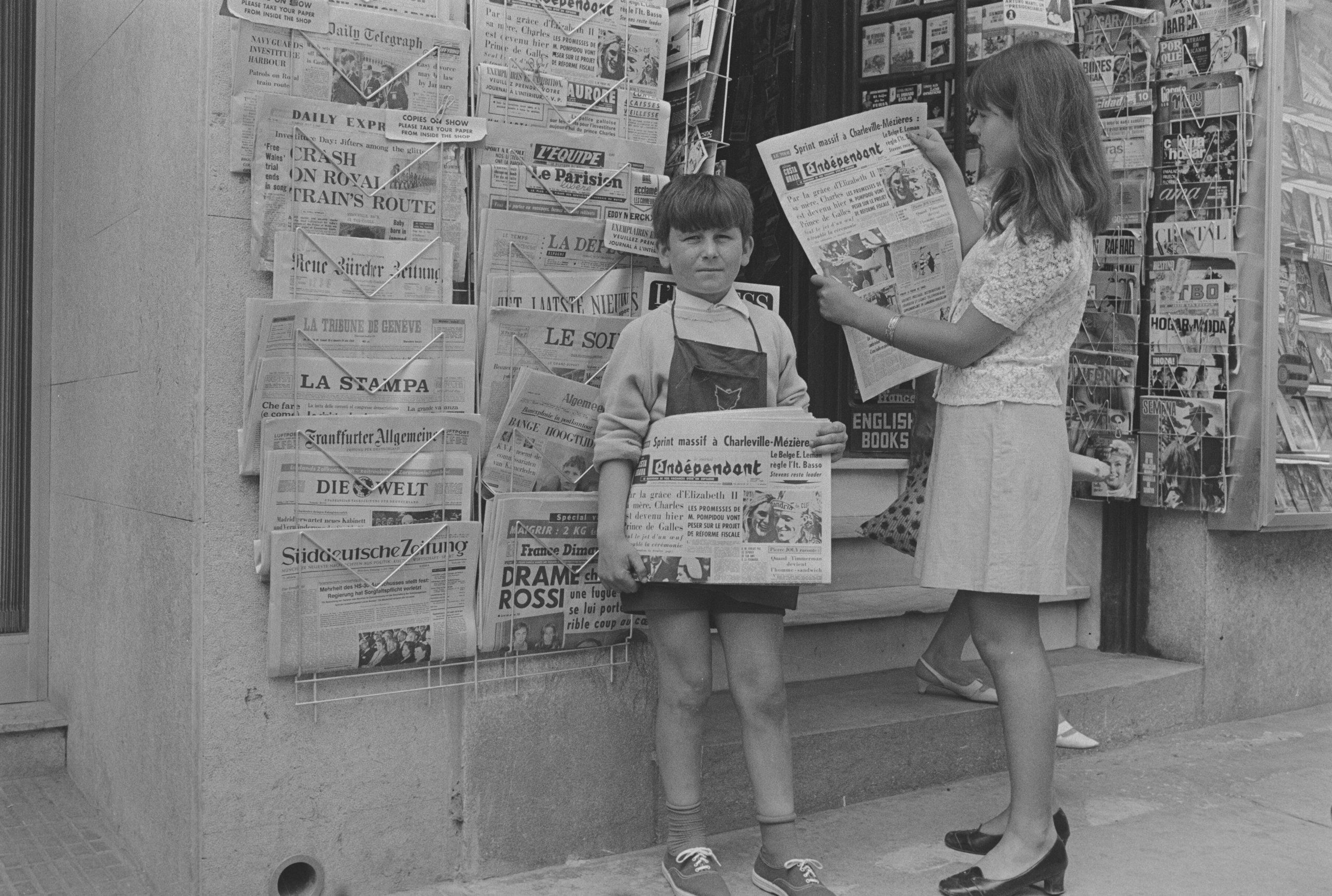 Niño y niña posando con las ediciones del diario «L’Indepéndant» frente a un quiosco